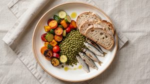 Assiette équilibrée vue du dessus avec légumes colorés, lentilles, sardines, pain complet et huile d’olive, éclairée par une lumière naturelle.